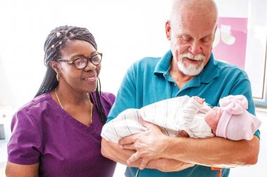 Older man holding a newborn as health care worker looks on