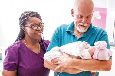 Anciano con un recién nacido como trabajador de la salud mira