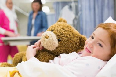 Child hugging a teddy bear in a hospital bed