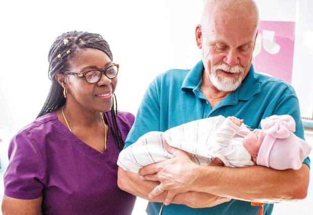 Older man holding a newborn as health care worker looks on