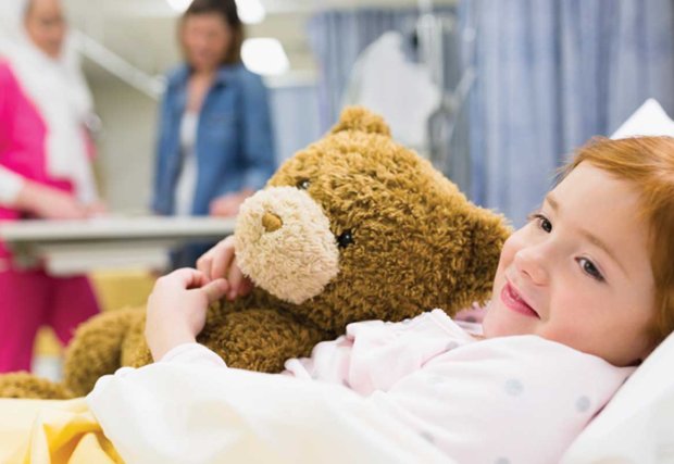Child hugging a teddy bear in a hospital bed