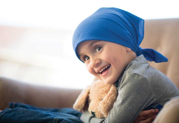 Paciente con cáncer infantil con pañuelo, sonriendo sosteniendo un oso de peluche