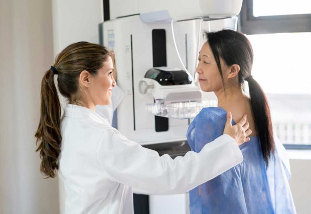 Woman being prepared for a mammogram by a smiling female health care staff person