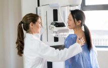 Woman being prepared for a mammogram by a smiling female health care staff person